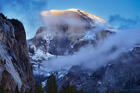 Half Dome in Yosemite Valley is shrouded in winter clouds and snow.