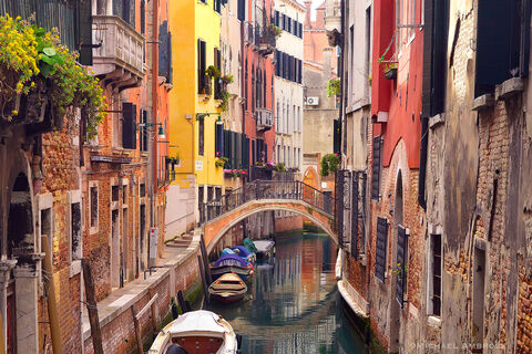 Beautifully weathered buildings and footbridges reflect in the brightly colored Venice canal.