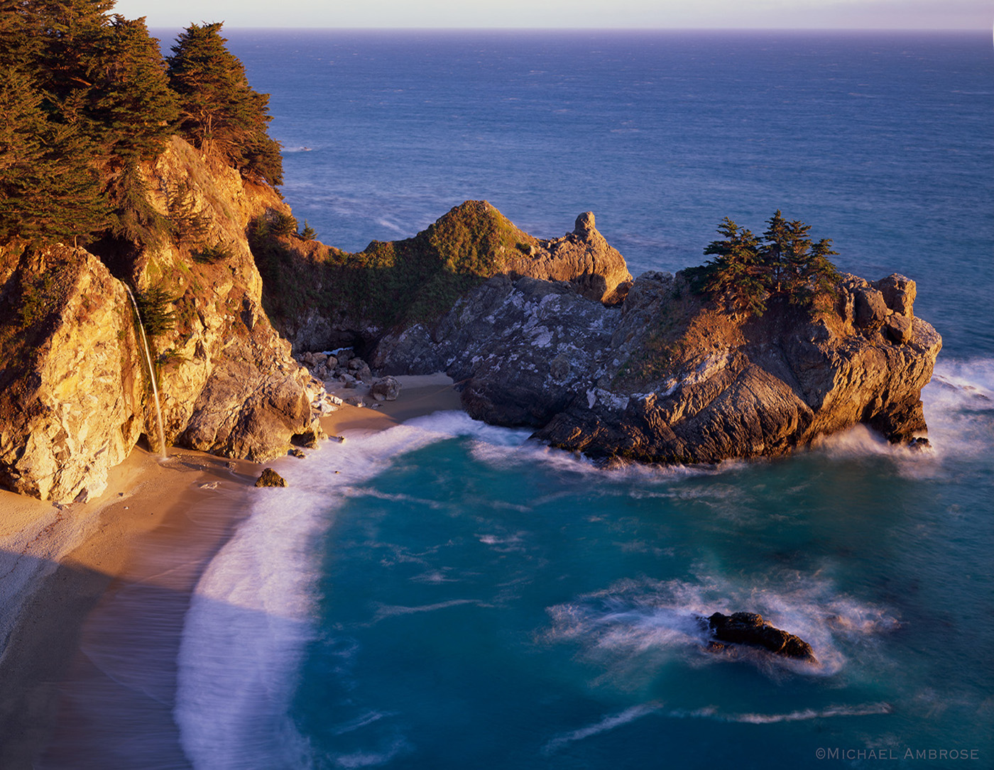 McWay Falls cascades onto golden sand lit by sunset light in the pristine cove at Julia Pfeiffer State Park in the Big Sur section of California coast. 