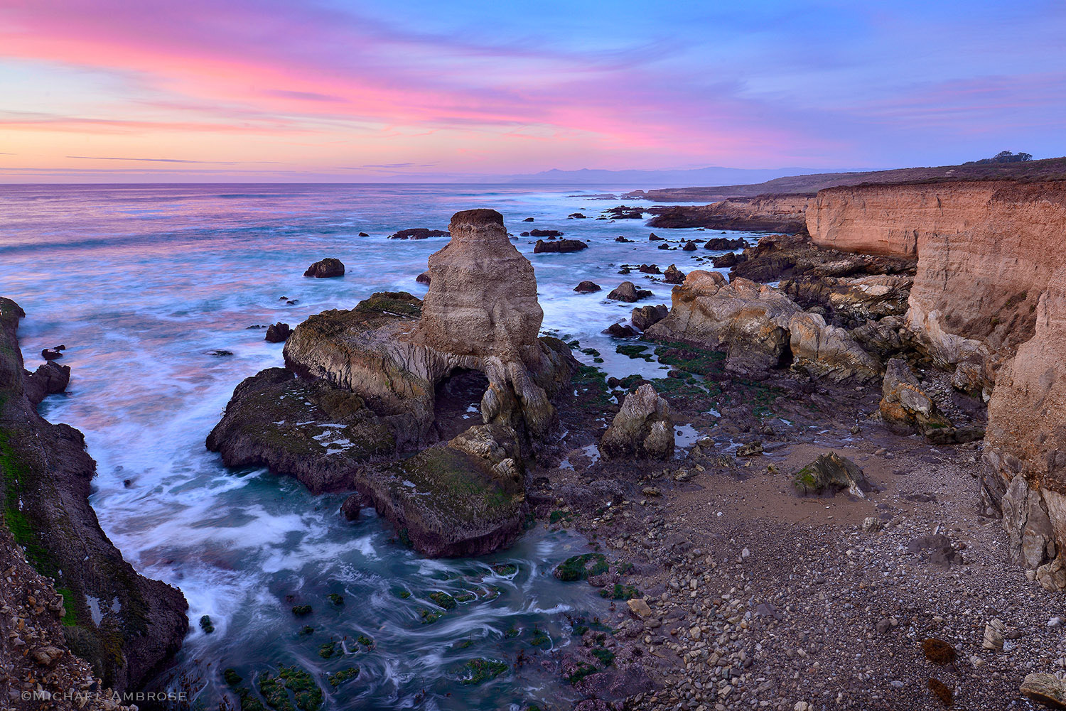 Evening sunset light paints the ocean and sky pink on the rocky cliffs of Montana de Oro State Park on the beautiful California coast.